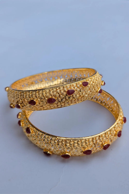 Pair of gold bangles with red stones on a light blue background