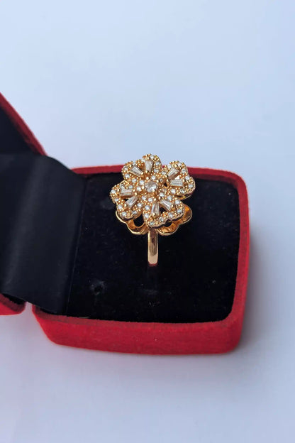 Gold ring with floral design in a red and black jewelry box on a light blue background