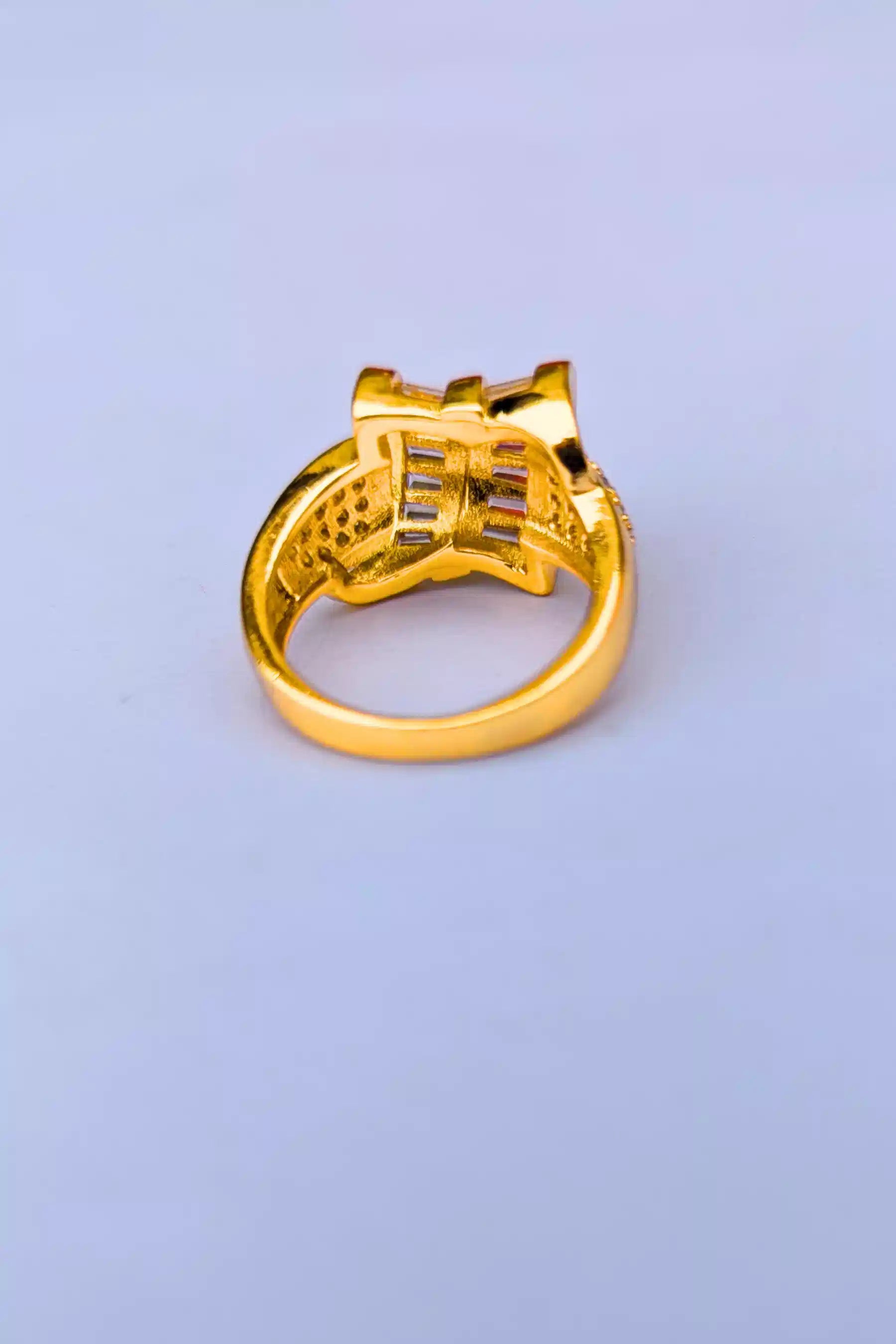 Gold ring with intricate design on a light purple background