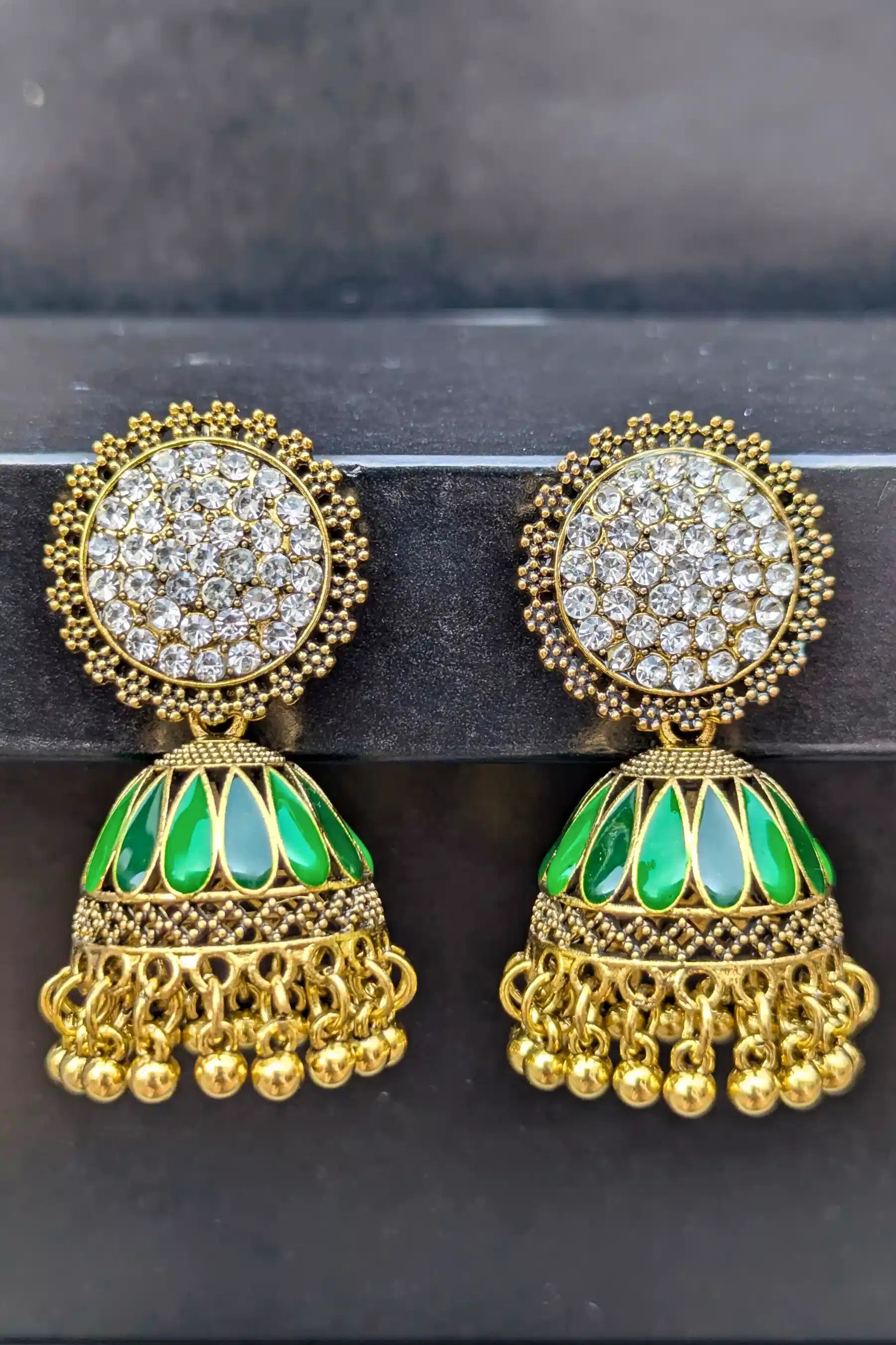 Gold and green earrings with intricate designs on a dark background