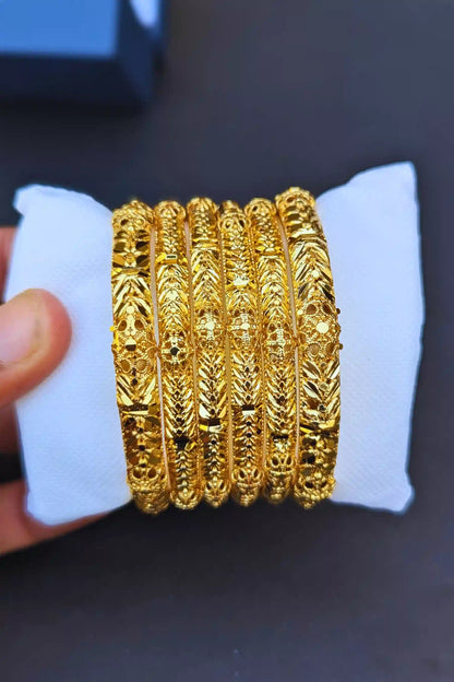 Set of gold bangles on a white stand with a dark background