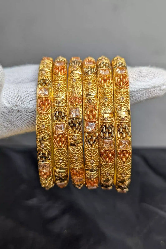 Set of gold bangles with intricate designs on a black background