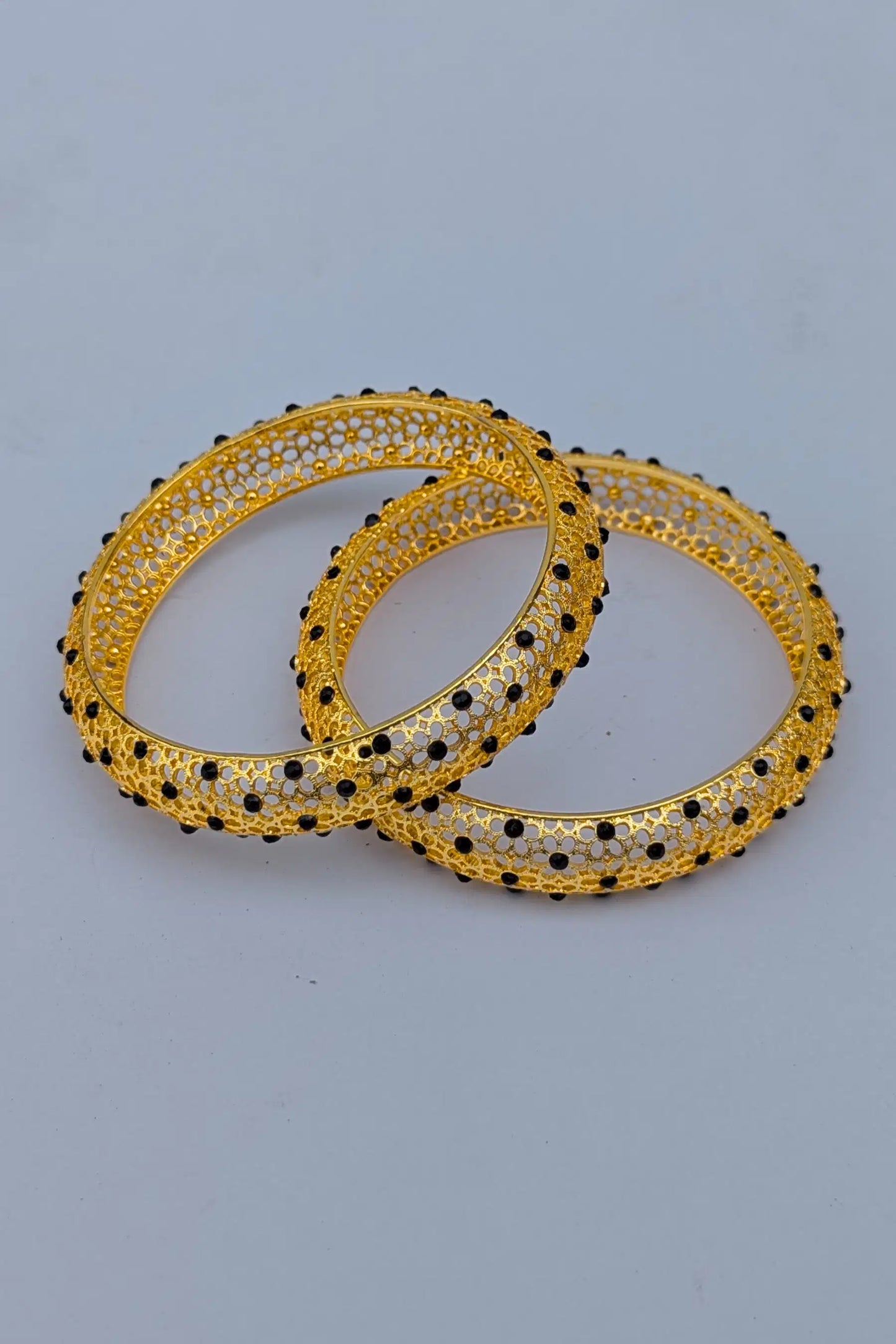 Pair of gold bangles with black beads on a light gray background