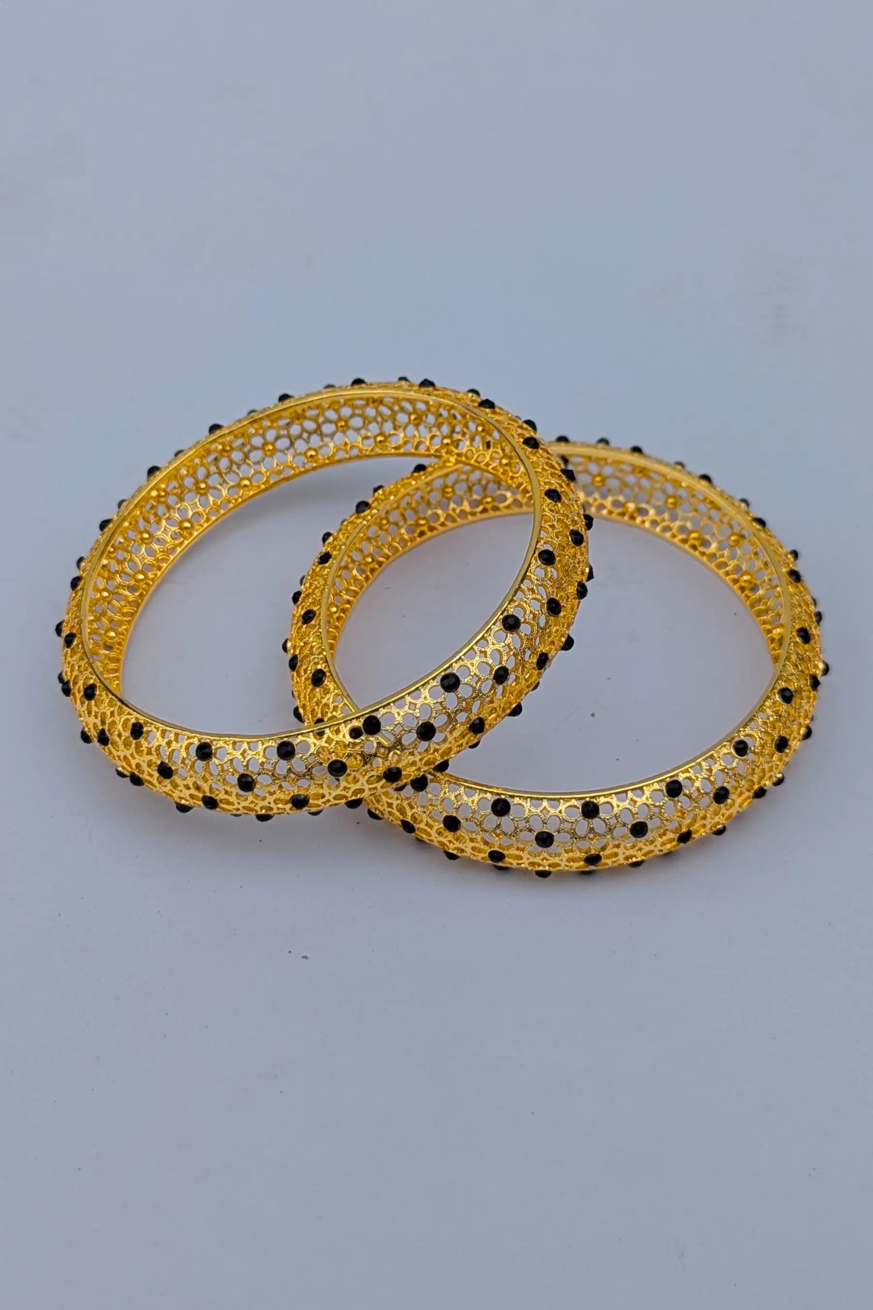 Pair of gold bangles with black beads on a light gray background