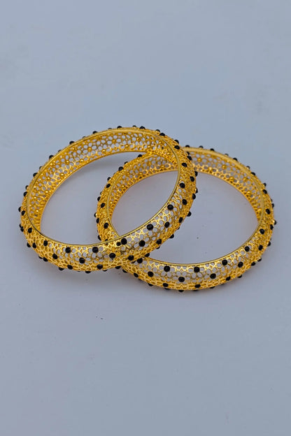 Pair of gold bangles with black beads on a light gray background