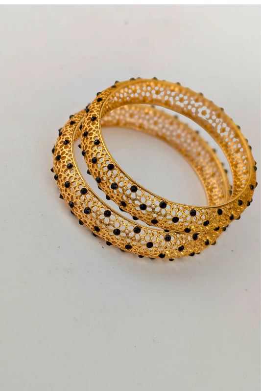 Gold bangles with black stones on a light gray background