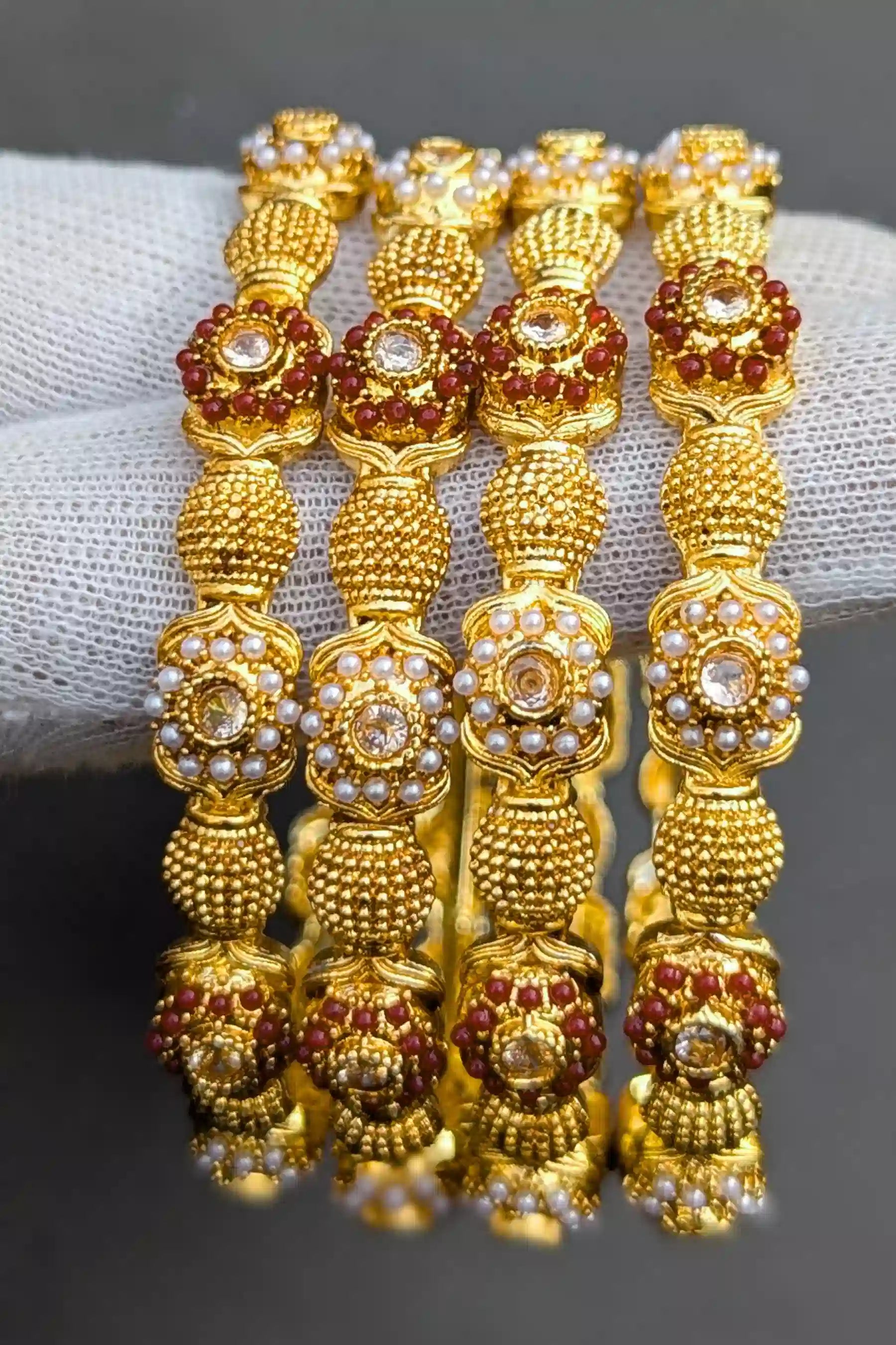 Gold bangles with red and white stones on a gray background