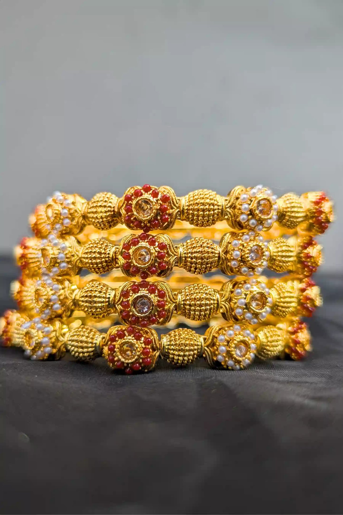 Set of gold bangles with intricate designs on a black surface