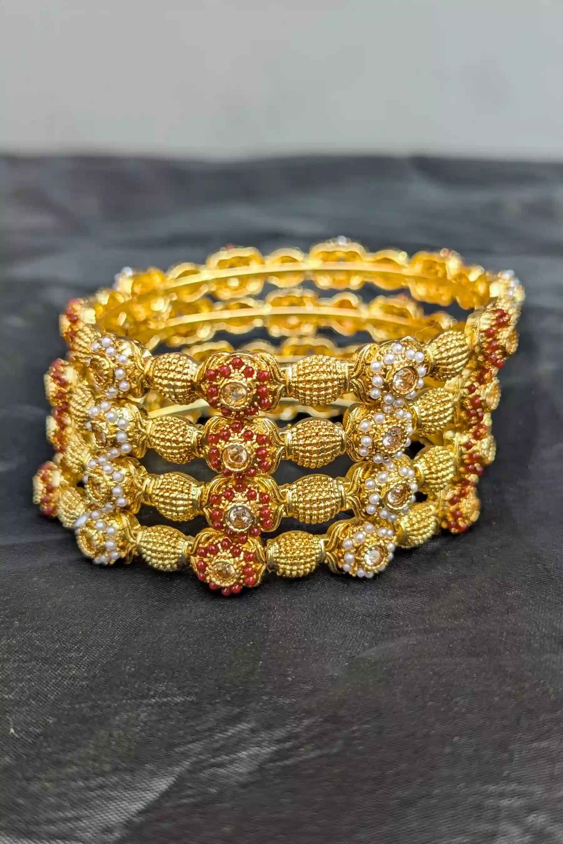 Set of gold bangles with floral designs on a dark surface