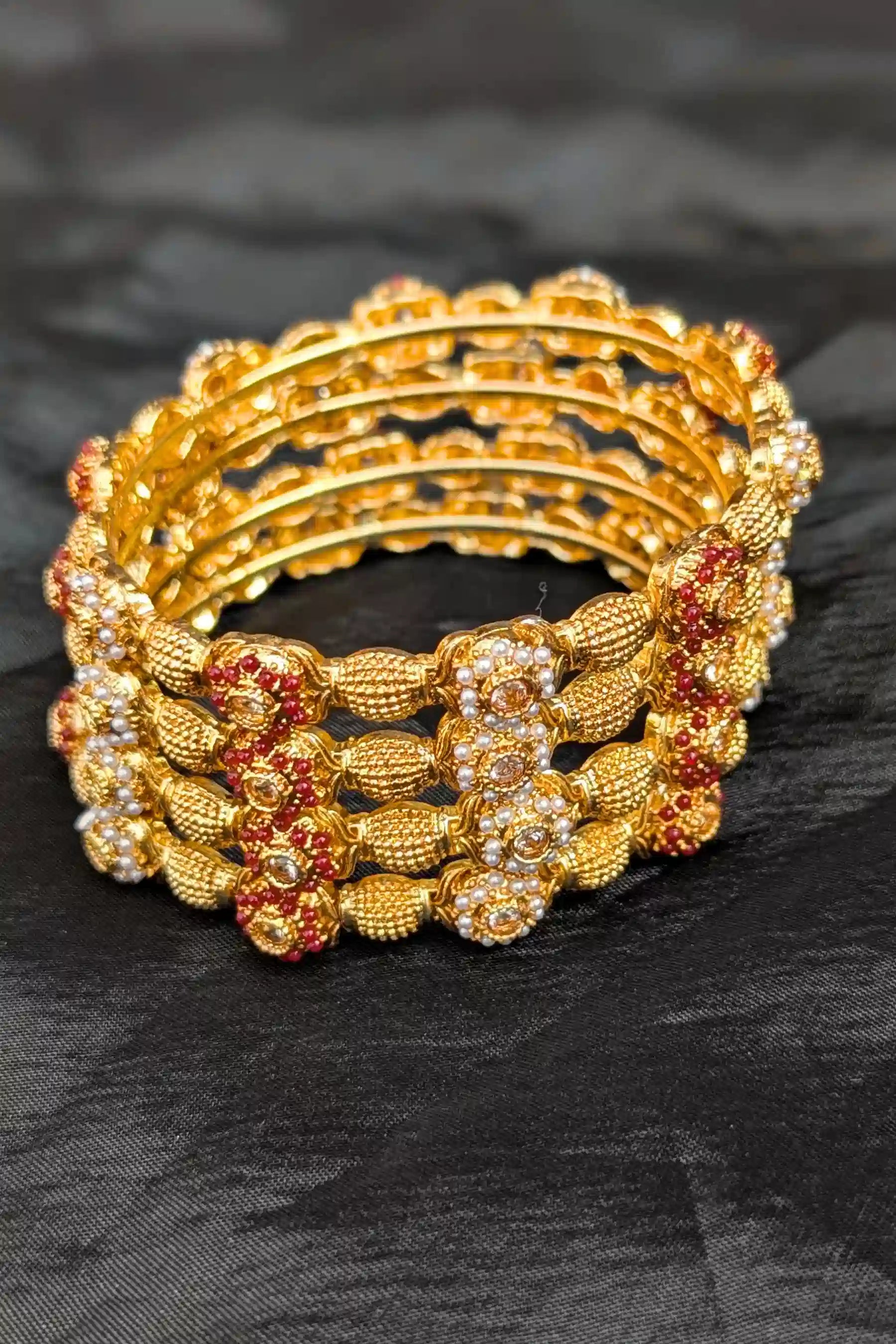 Set of gold and red beaded bracelets on a black fabric background
