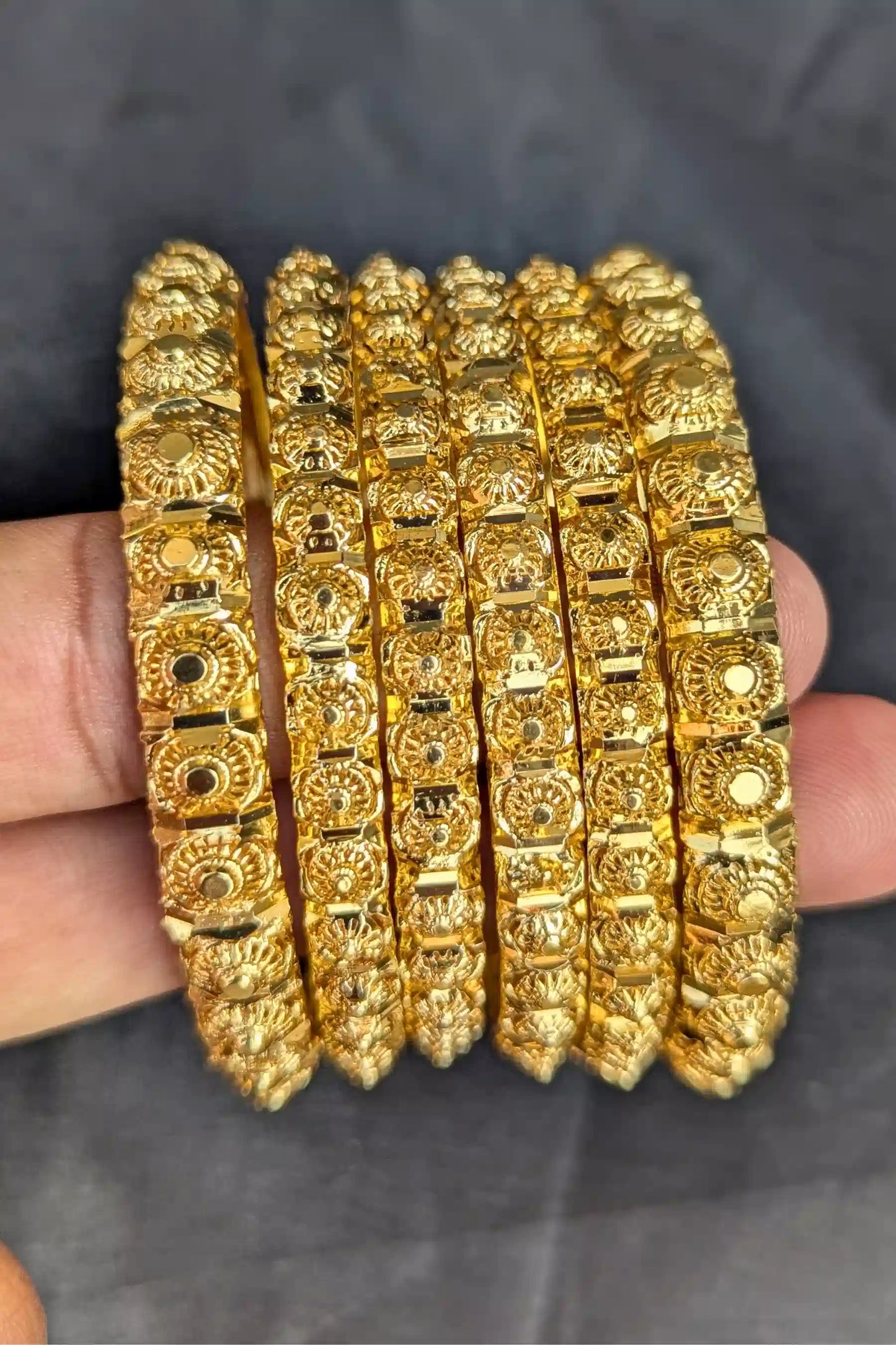 Set of gold bangles held by a hand against a dark background