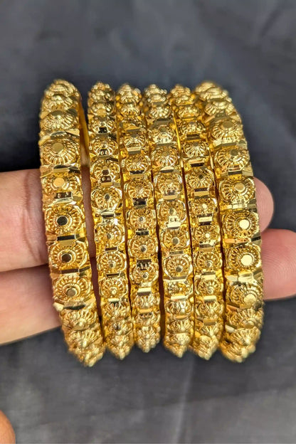 Set of gold bangles held by a hand against a dark background
