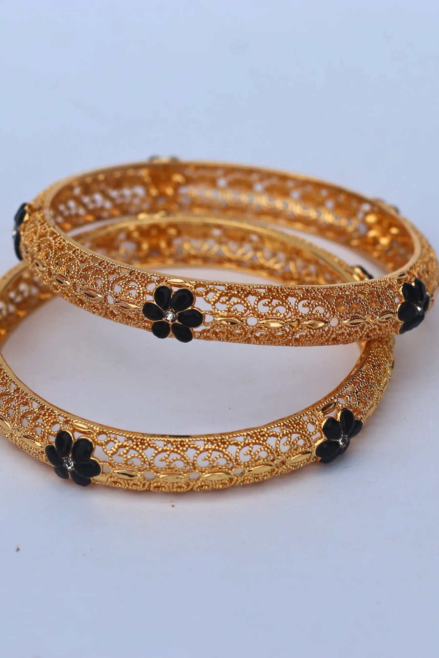 Gold bangles with black floral accents on a light gray background