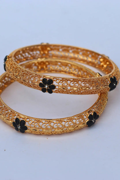 Gold bangles with black floral accents on a light gray background