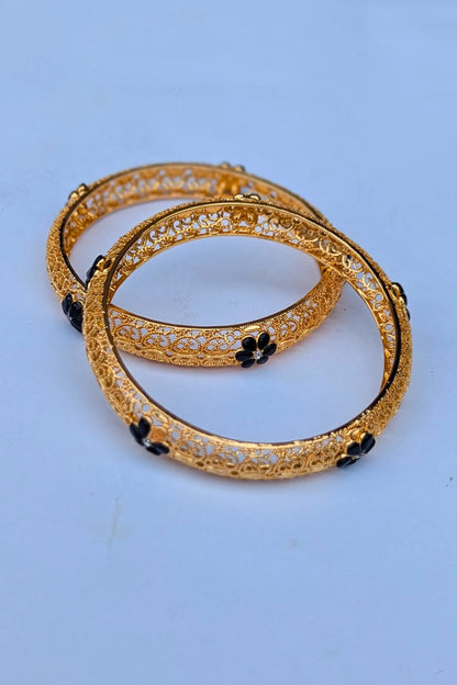 Two gold bangles with black stones on a light blue background