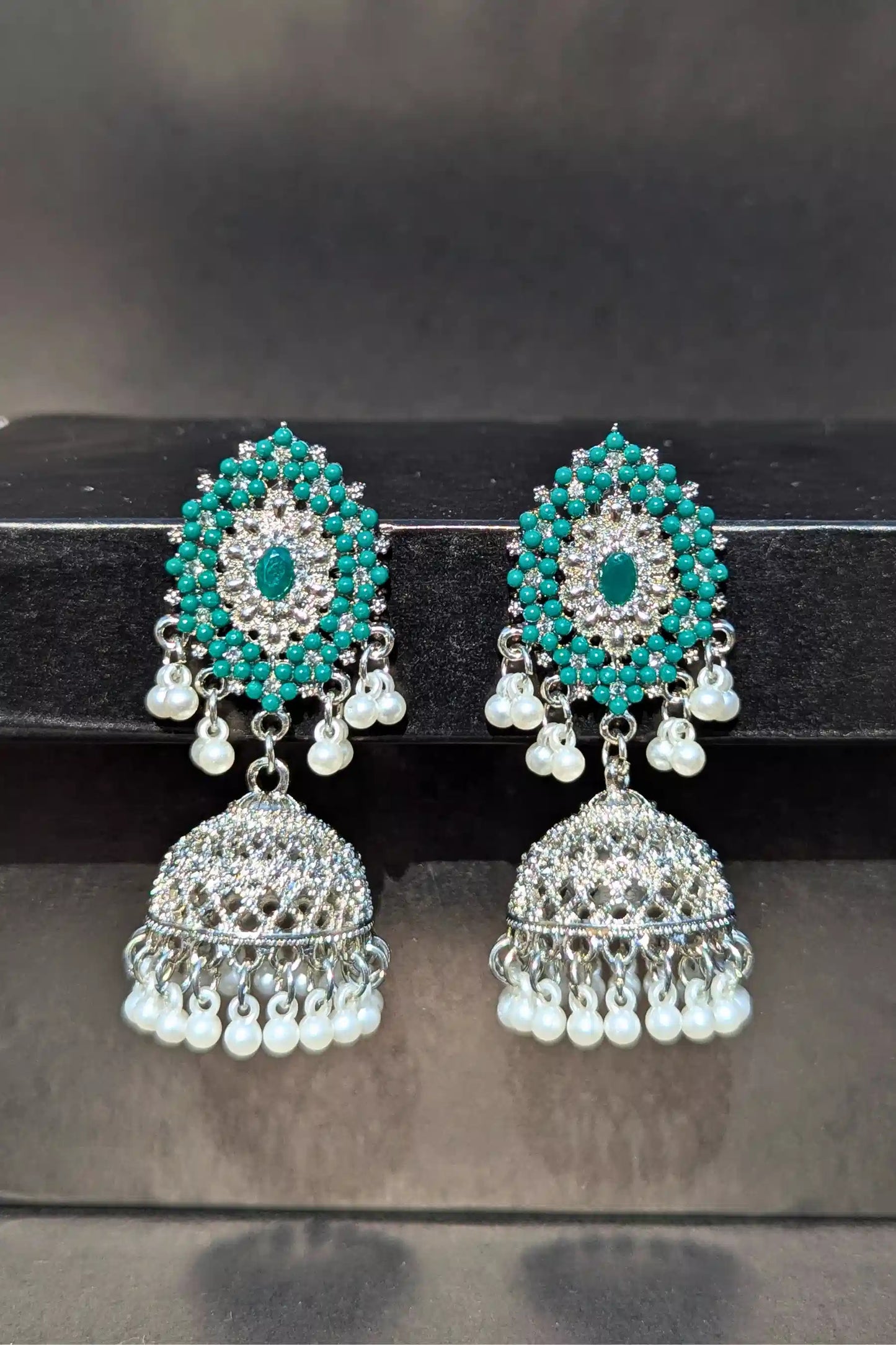 Pair of turquoise and pearl earrings on a black stand