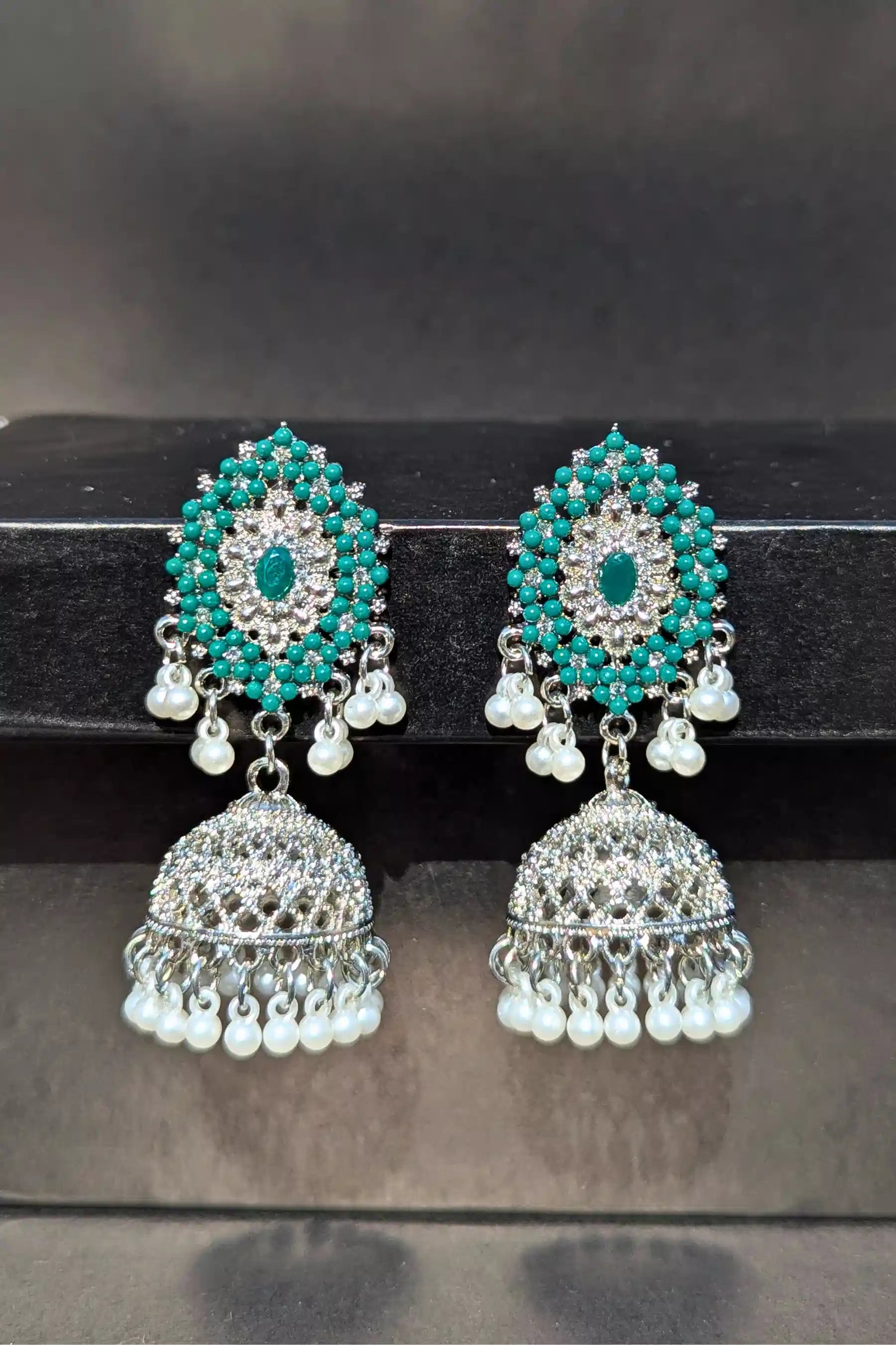 Pair of turquoise and pearl earrings on a black stand