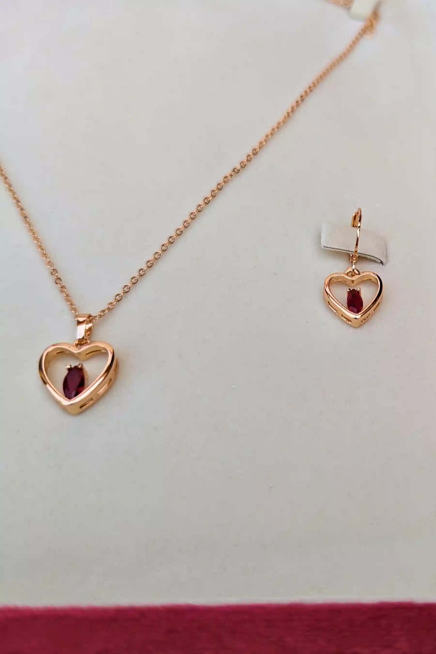 Rose gold heart-shaped jewelry set with red gemstones on a white background