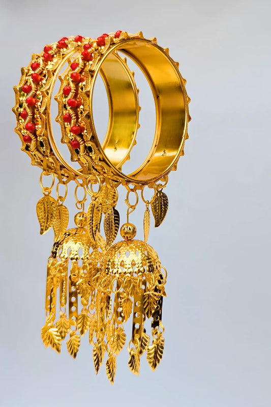 Gold bangles with red stones and dangling elements on a light gray background
