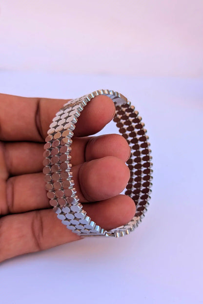 Silver beaded bracelet held by a hand on a white background
