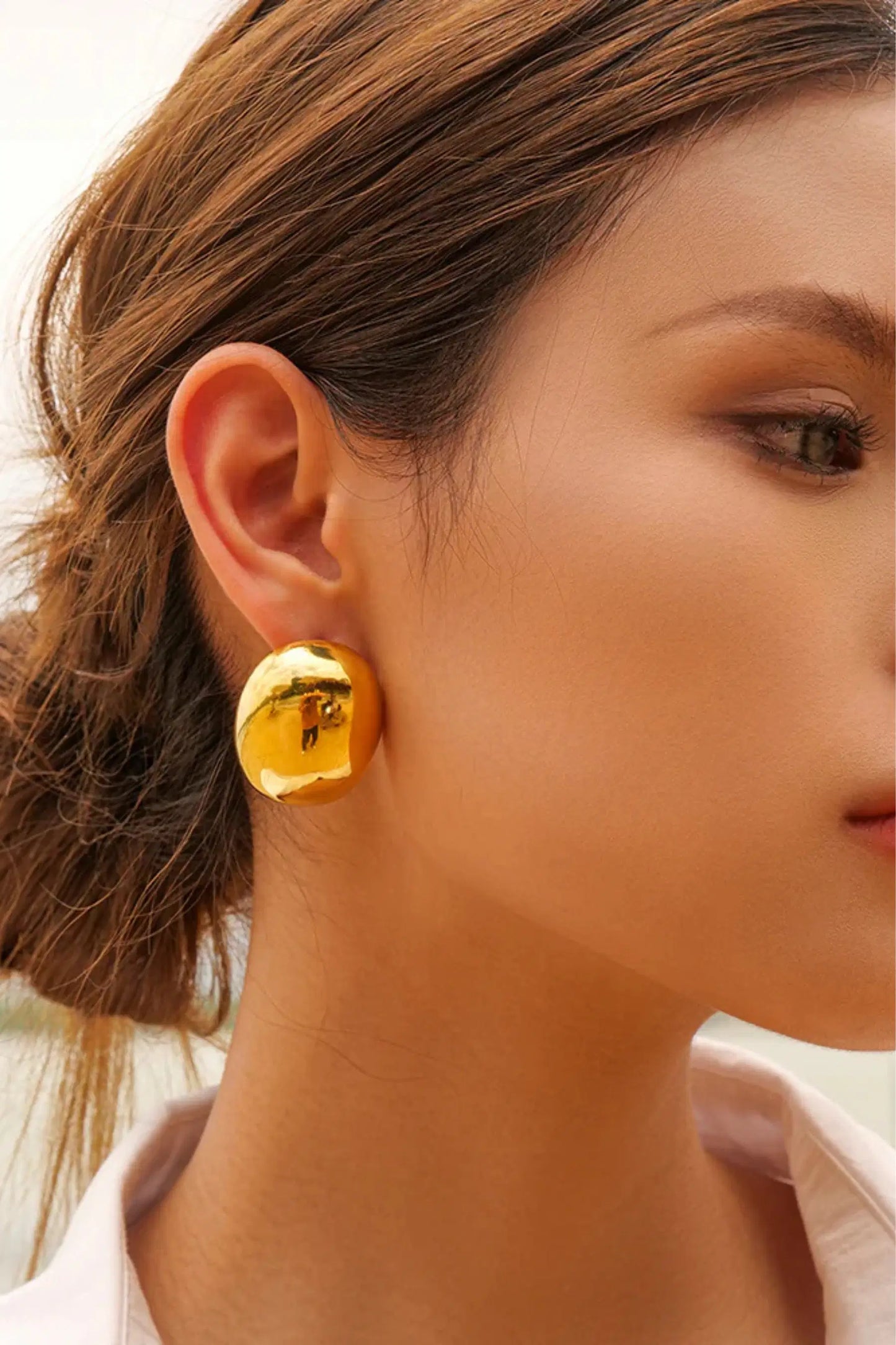Close-up of a person wearing a gold earring with a blurred background