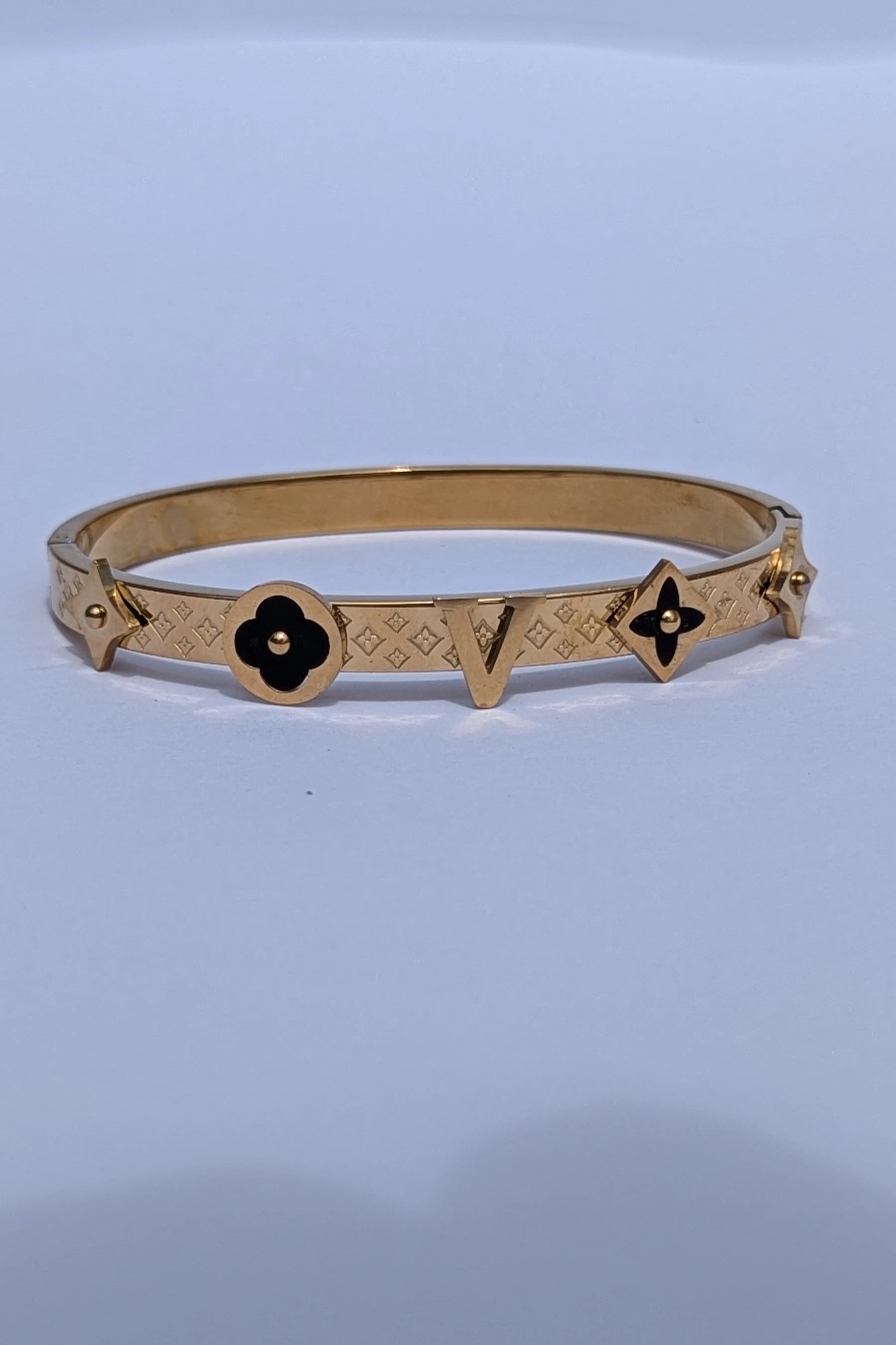 Gold bracelet with black flower designs on a light blue background