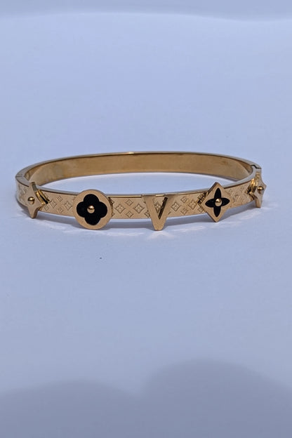 Gold bracelet with black flower designs on a light blue background
