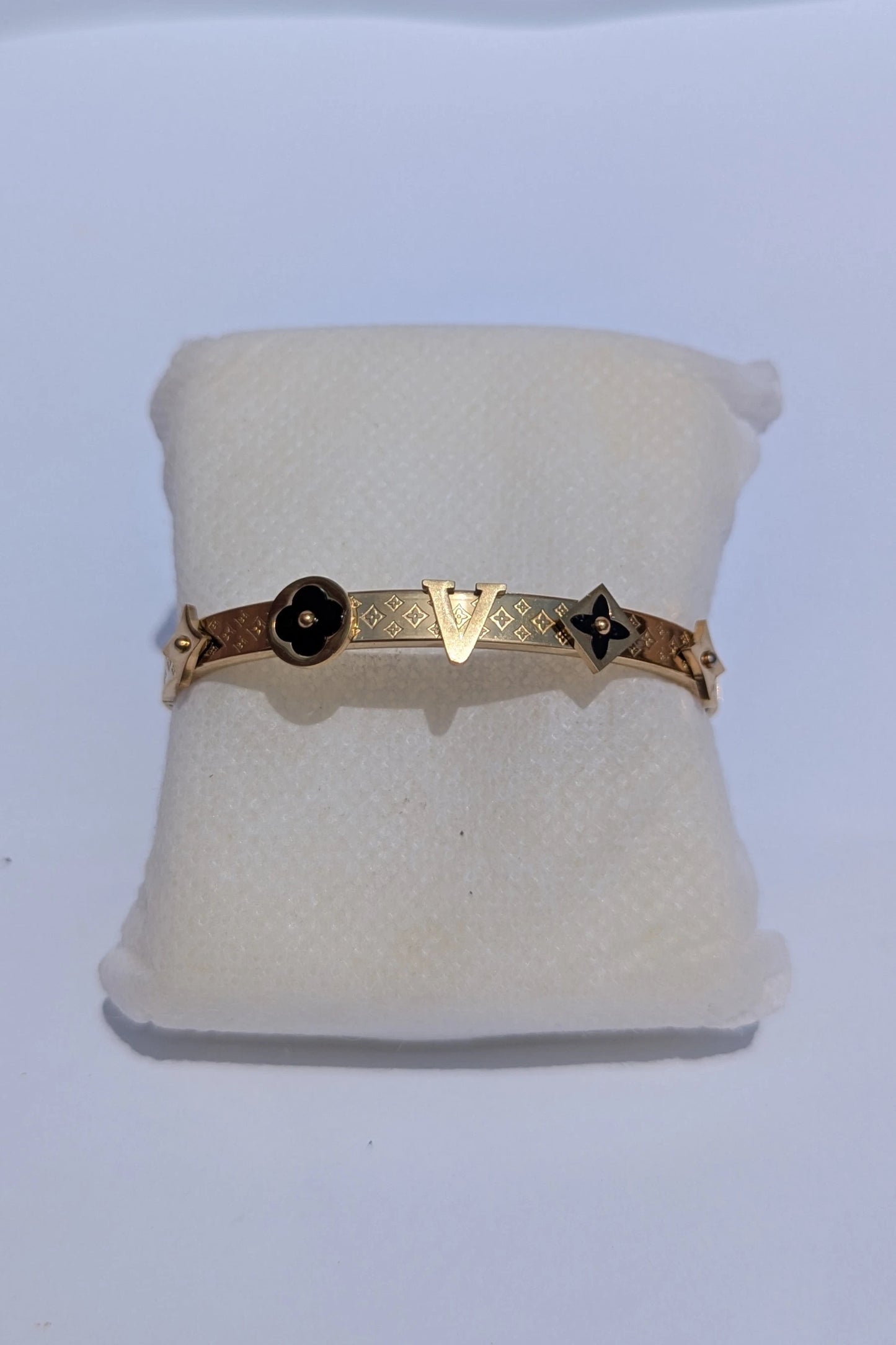 Gold bracelet with black stones on a white cushion against a white background