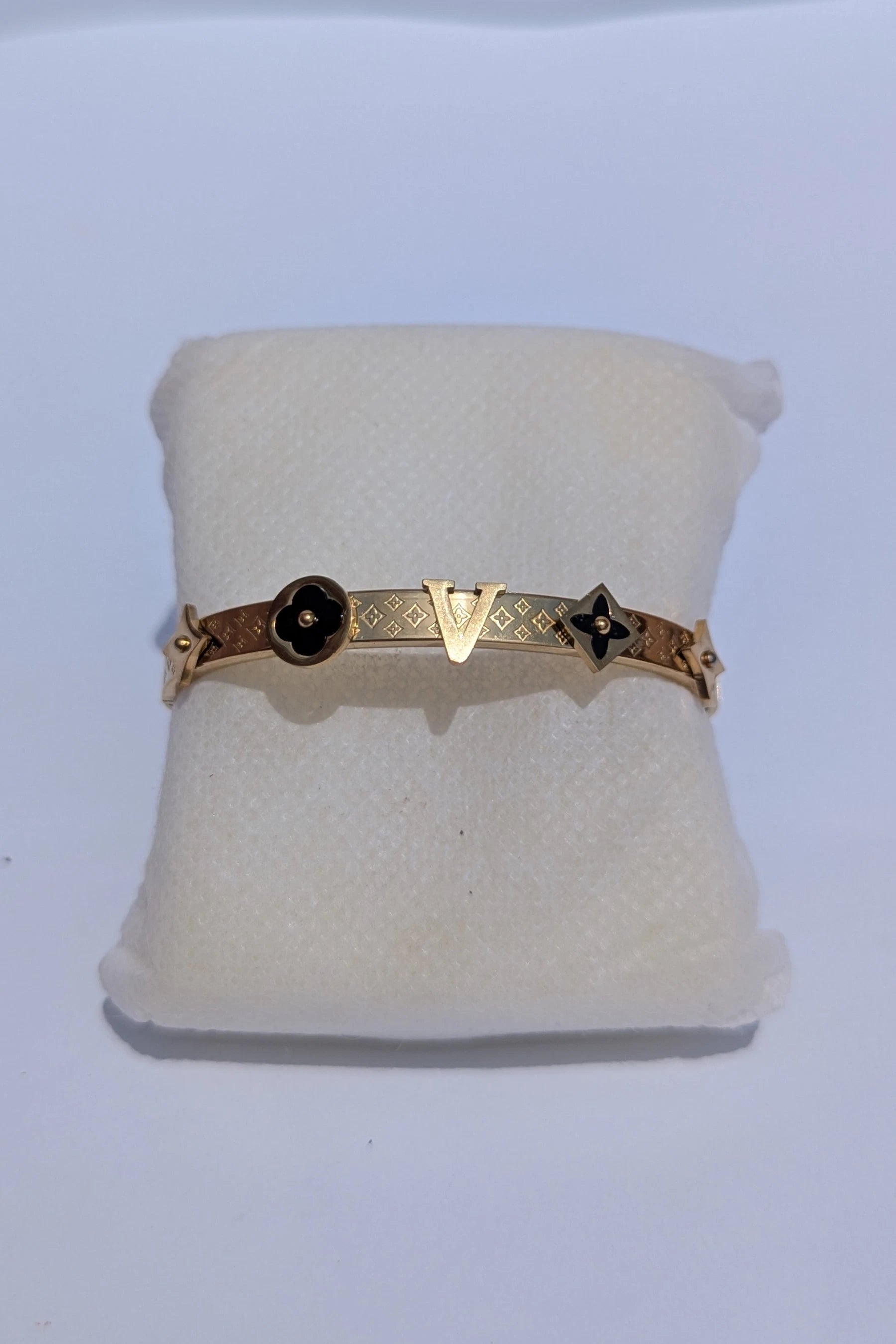 Gold bracelet with black stones on a white cushion against a white background