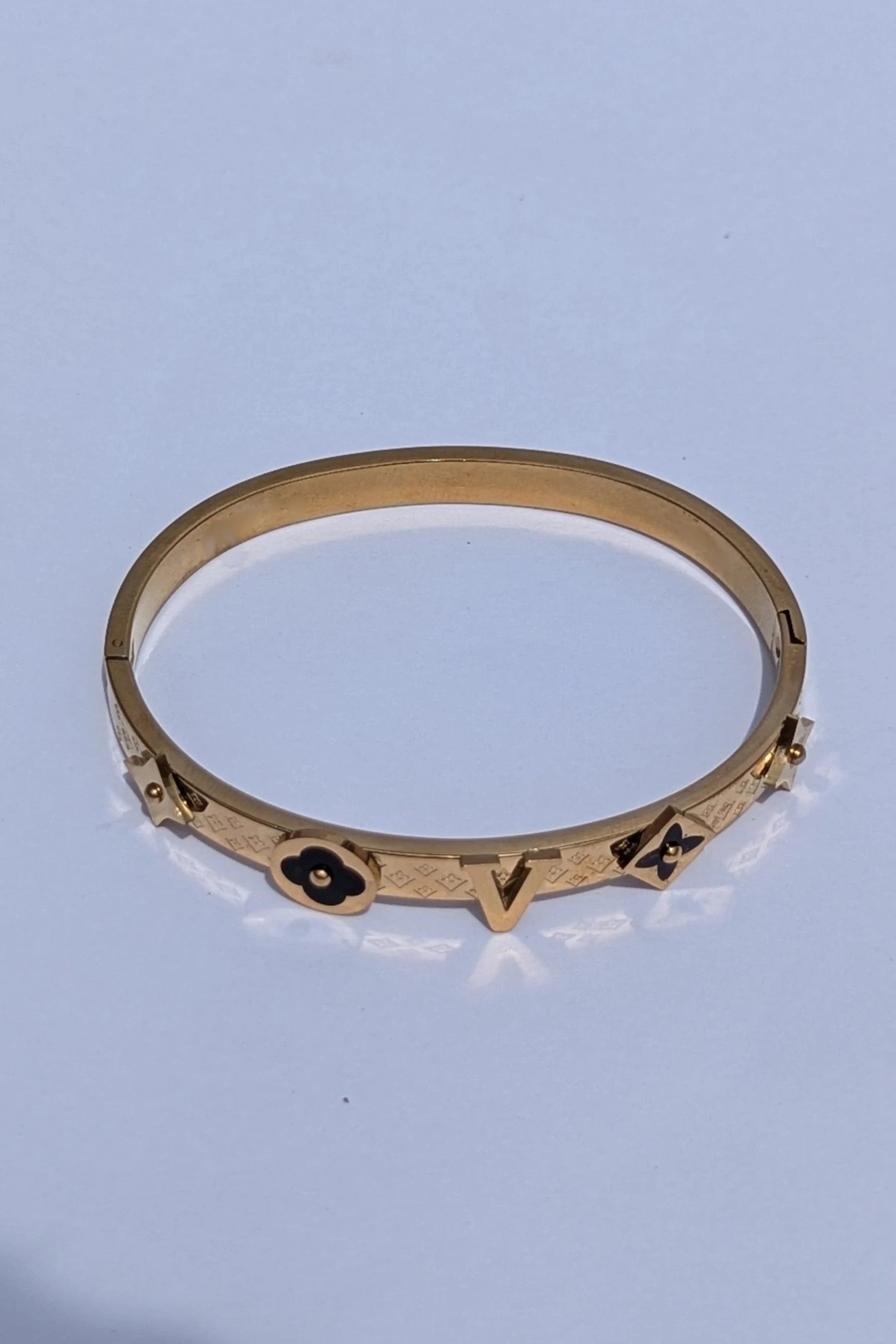 Gold bracelet with engraved symbols on a light blue background