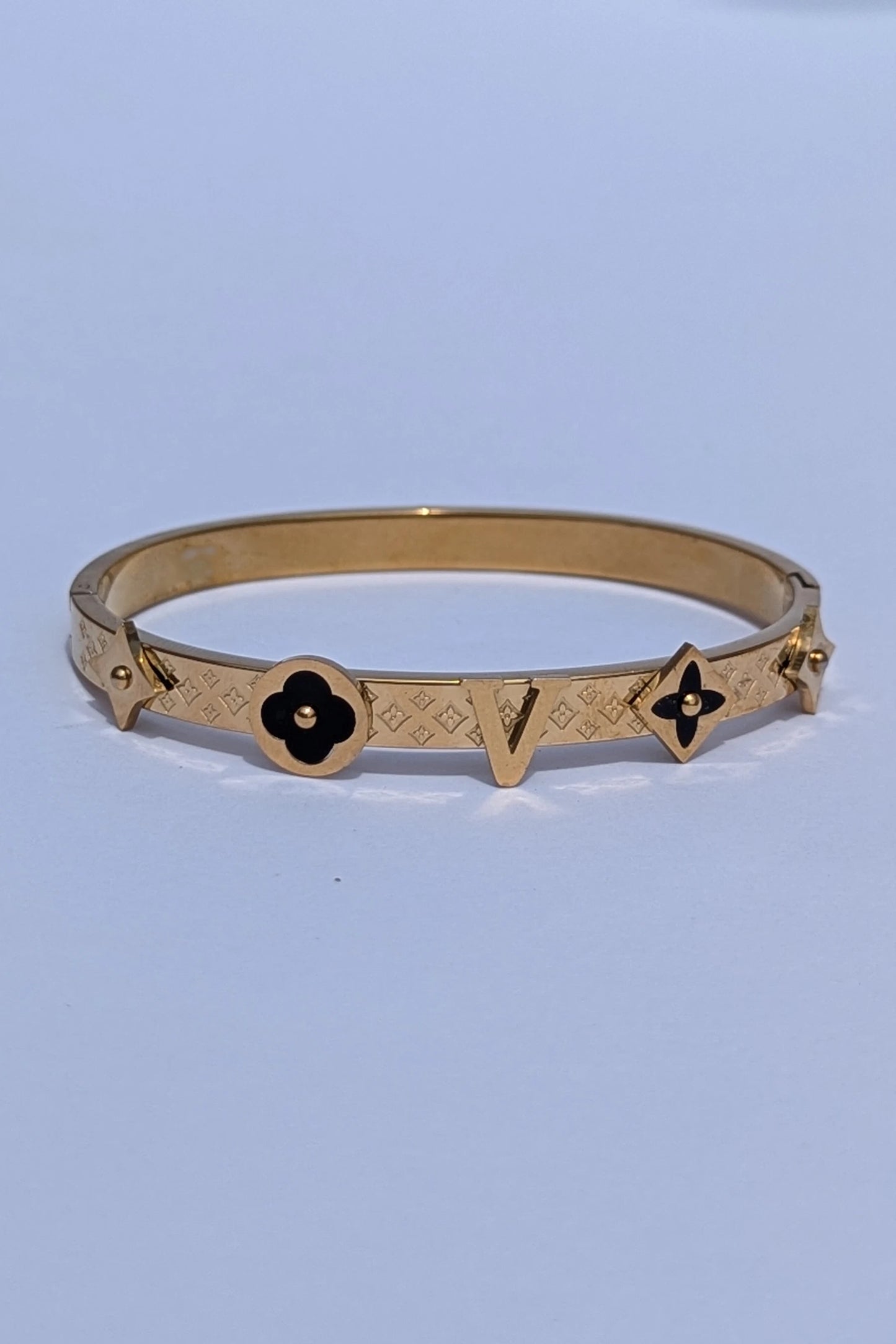 Gold bracelet with black flower designs on a light blue background