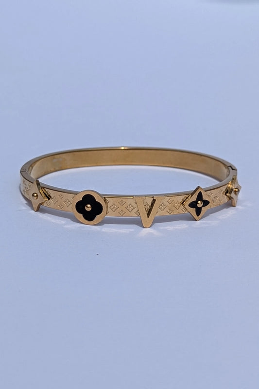 Gold bracelet with black flower designs on a light blue background