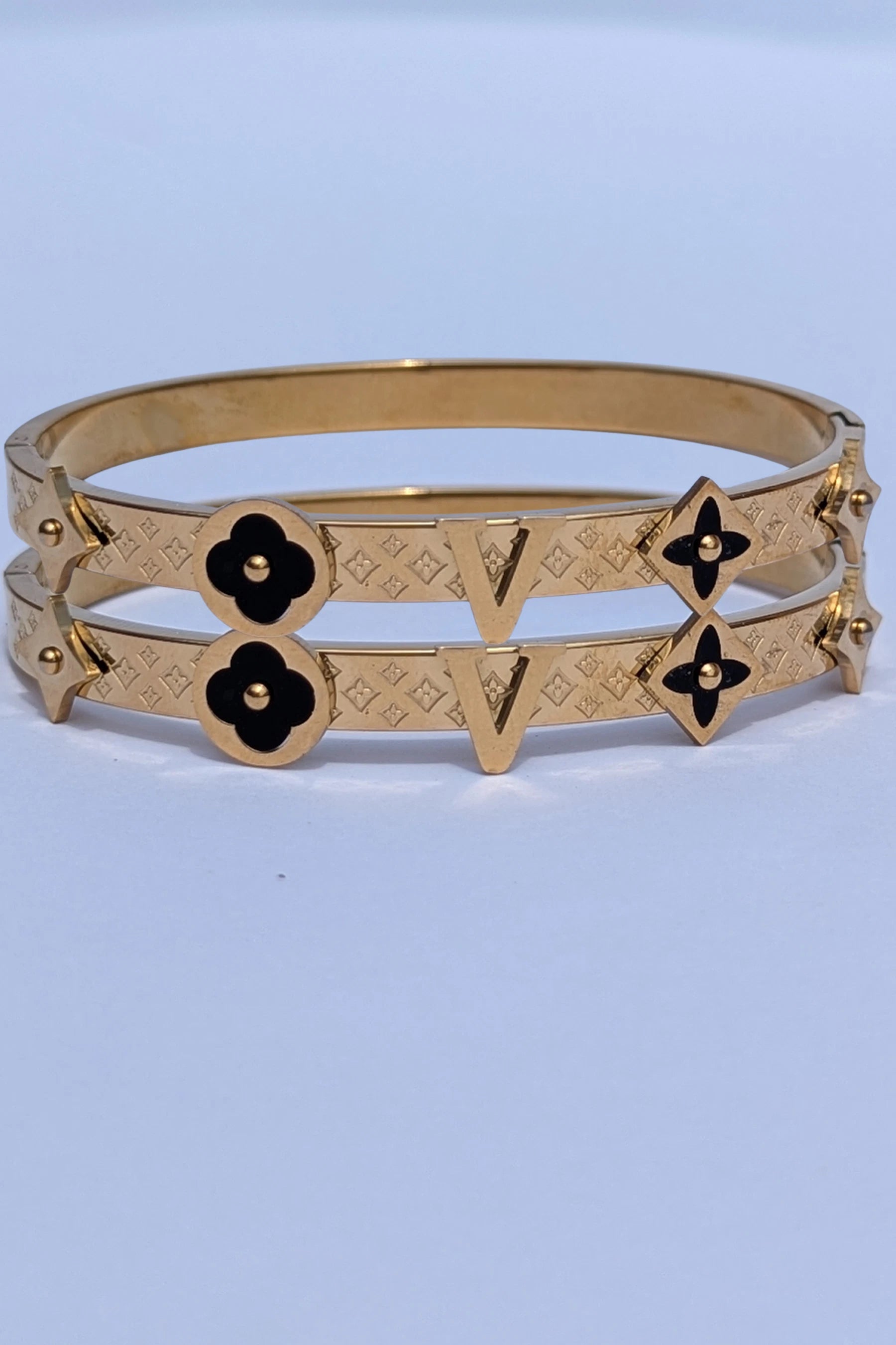 Gold bracelet with black flower designs on a light blue background