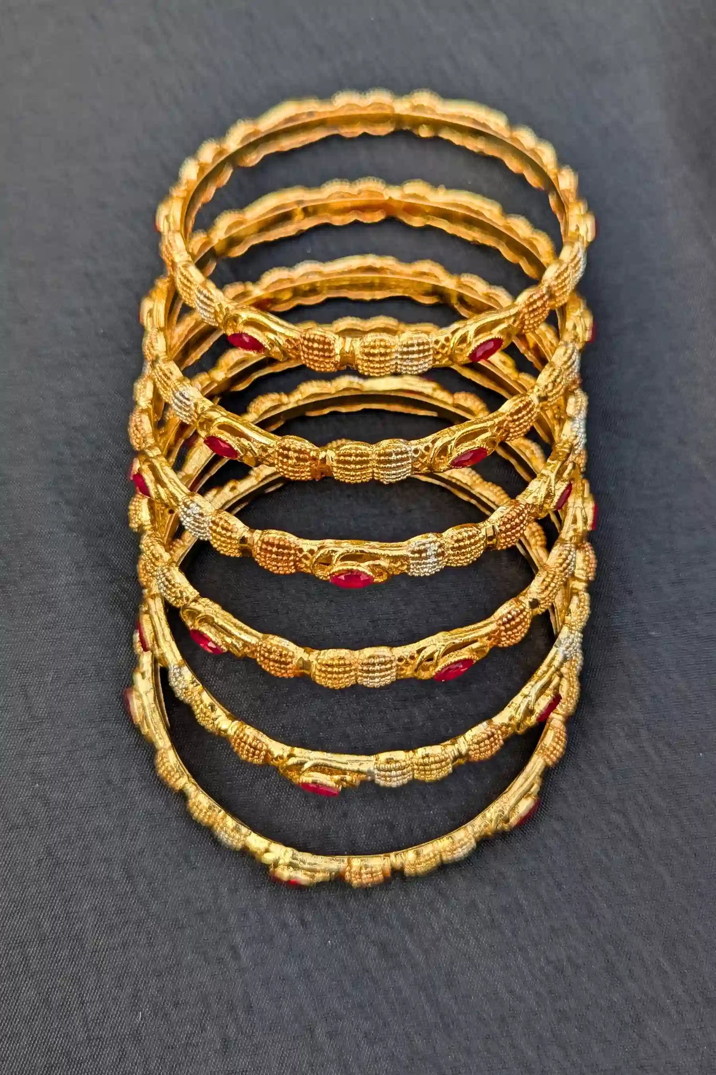 Stack of gold bangles with red stones on a dark gray background