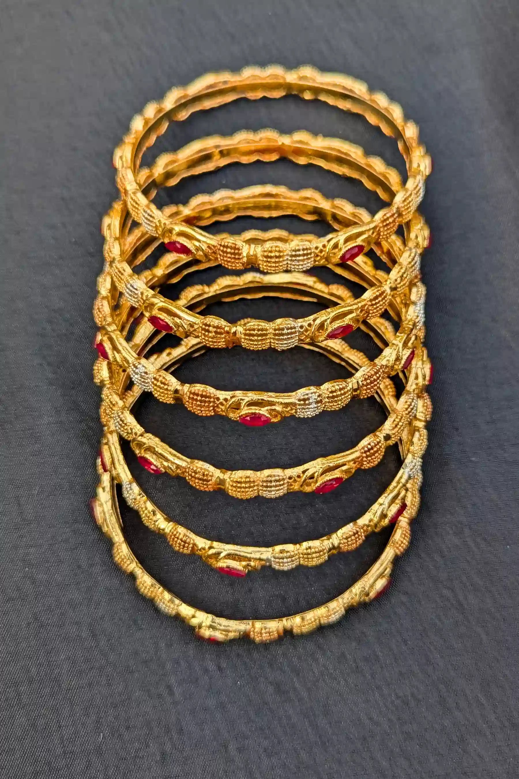 Stack of gold bangles with red stones on a dark gray background