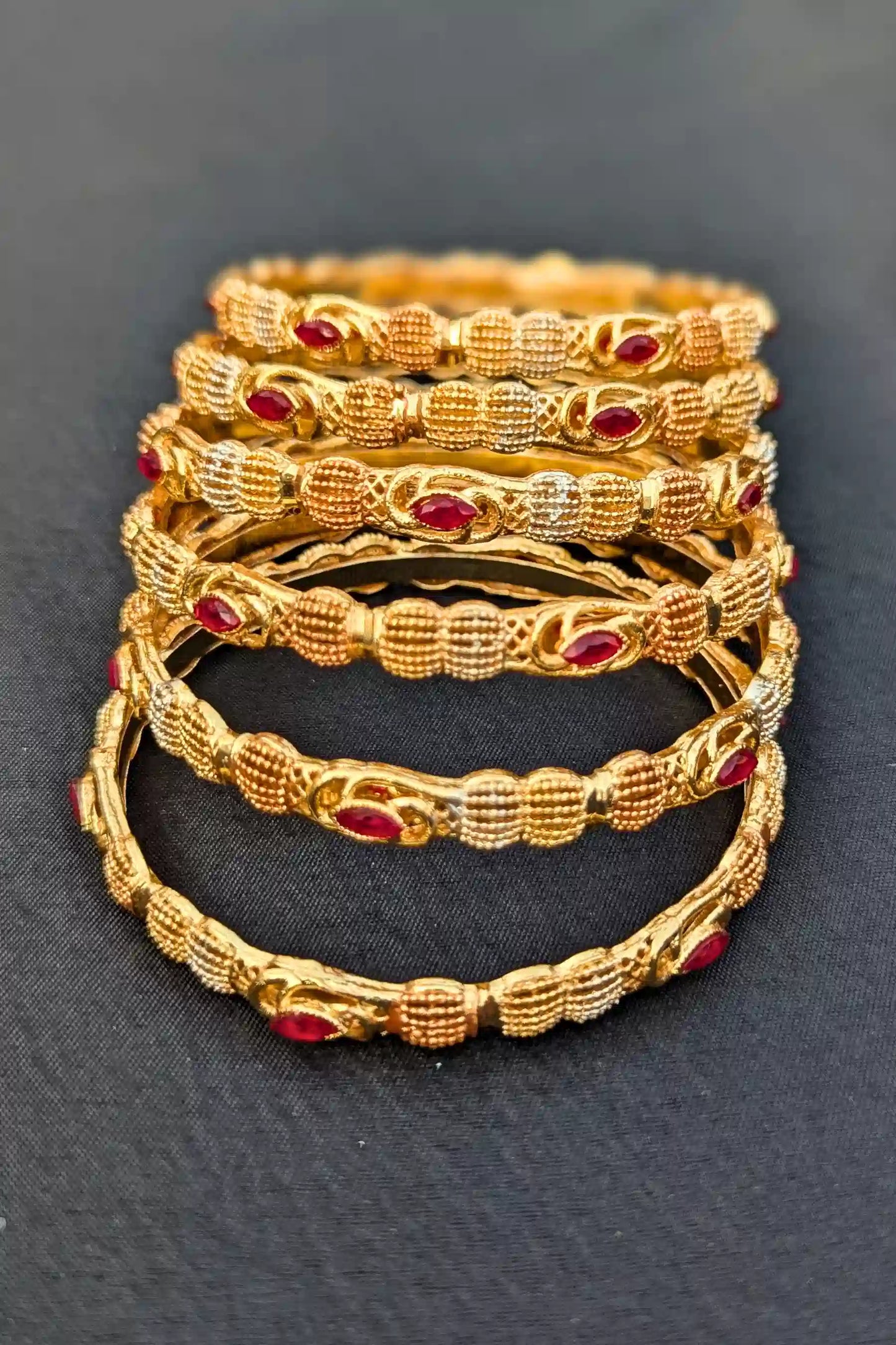 Set of gold bangles with red stones on a dark background
