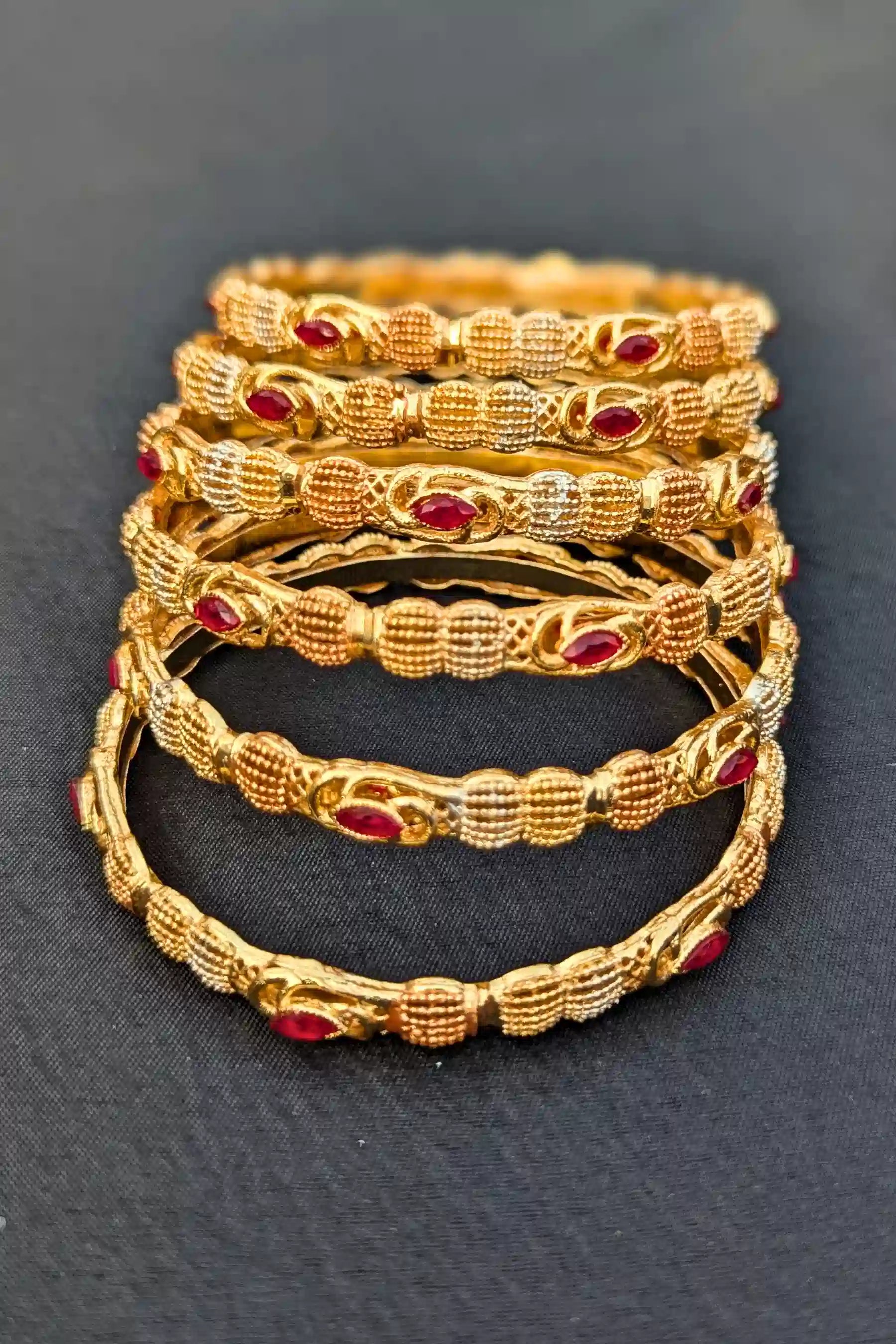 Set of gold bangles with red stones on a dark background
