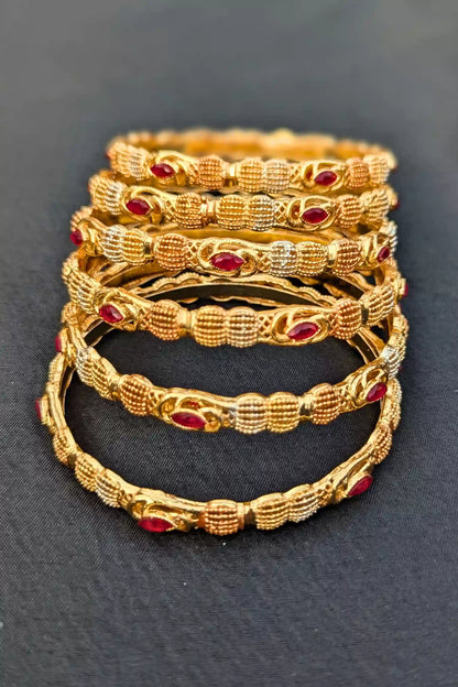 Set of gold bangles with red stones on a dark background