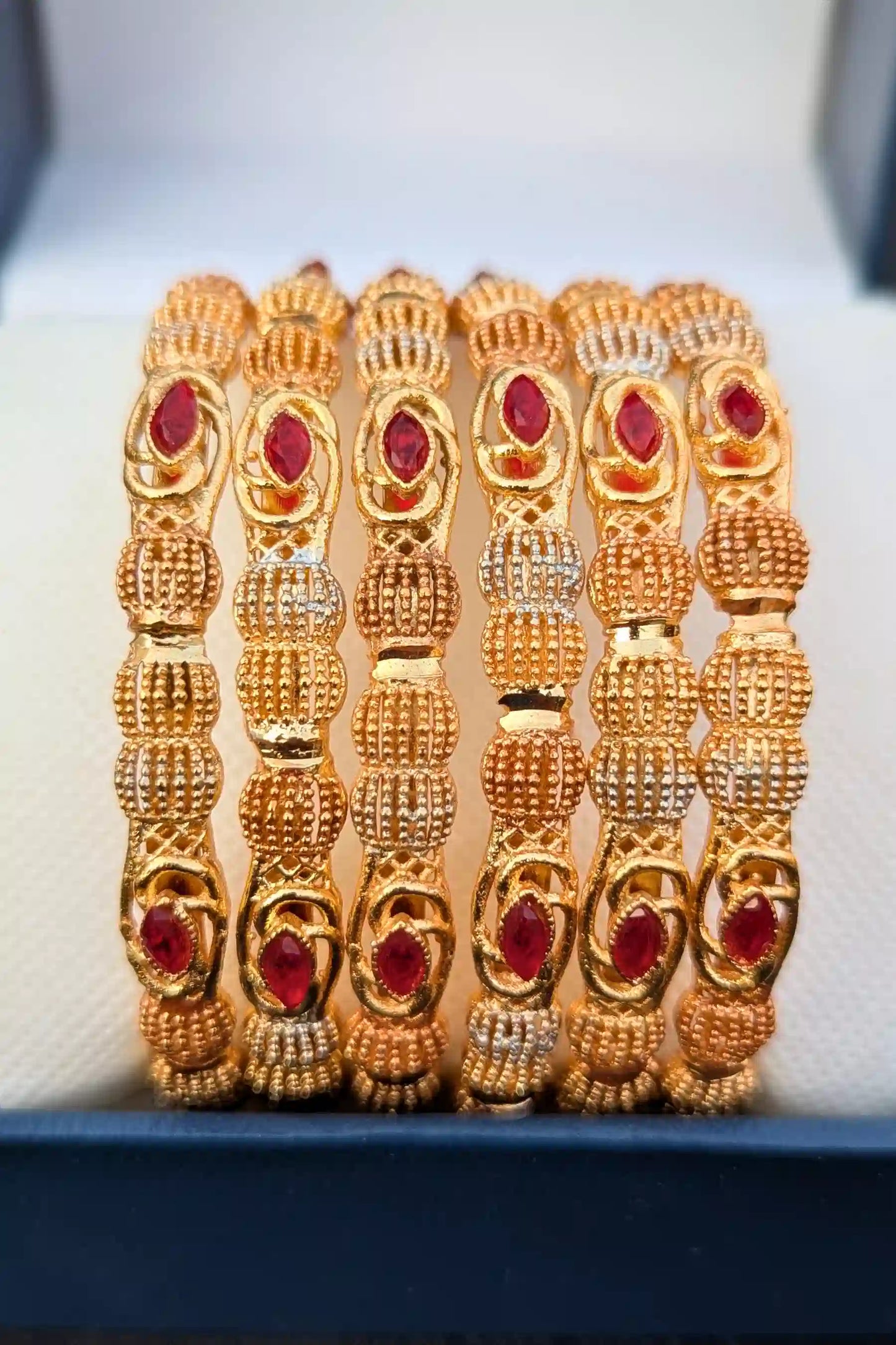 Set of gold bangles with red stones on a white background
