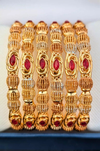 Set of gold bangles with red stones on a white background
