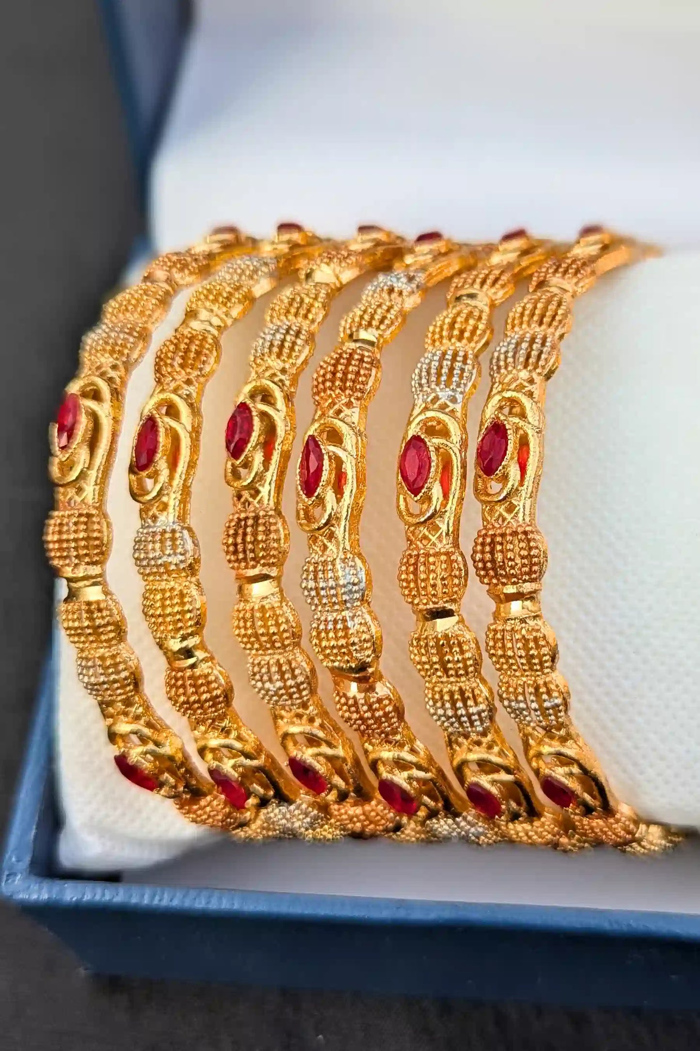 Set of gold bangles with red stones on a white surface