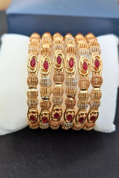Set of gold bangles with red stones on a black surface