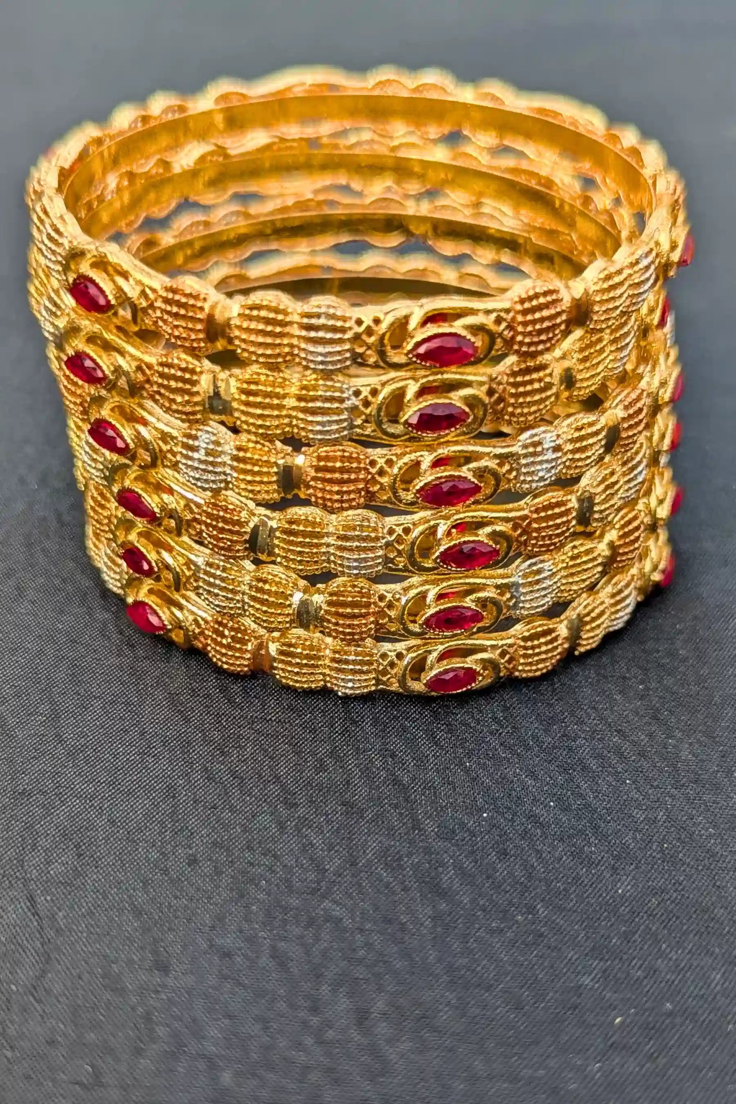 Set of gold bangles with red stones on a dark fabric background