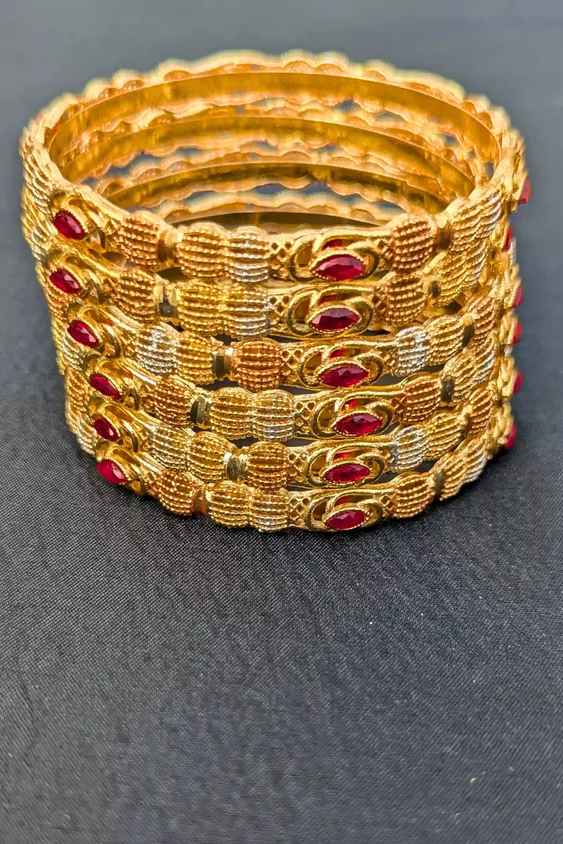 Set of gold bangles with red stones on a dark fabric background