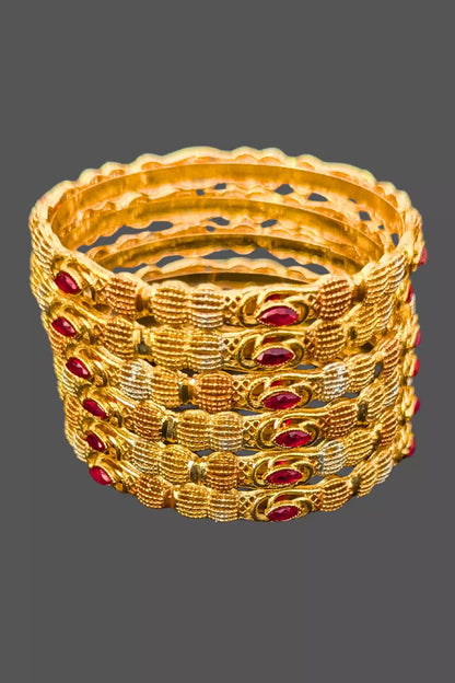 Set of gold bangles with red stones on a gray background