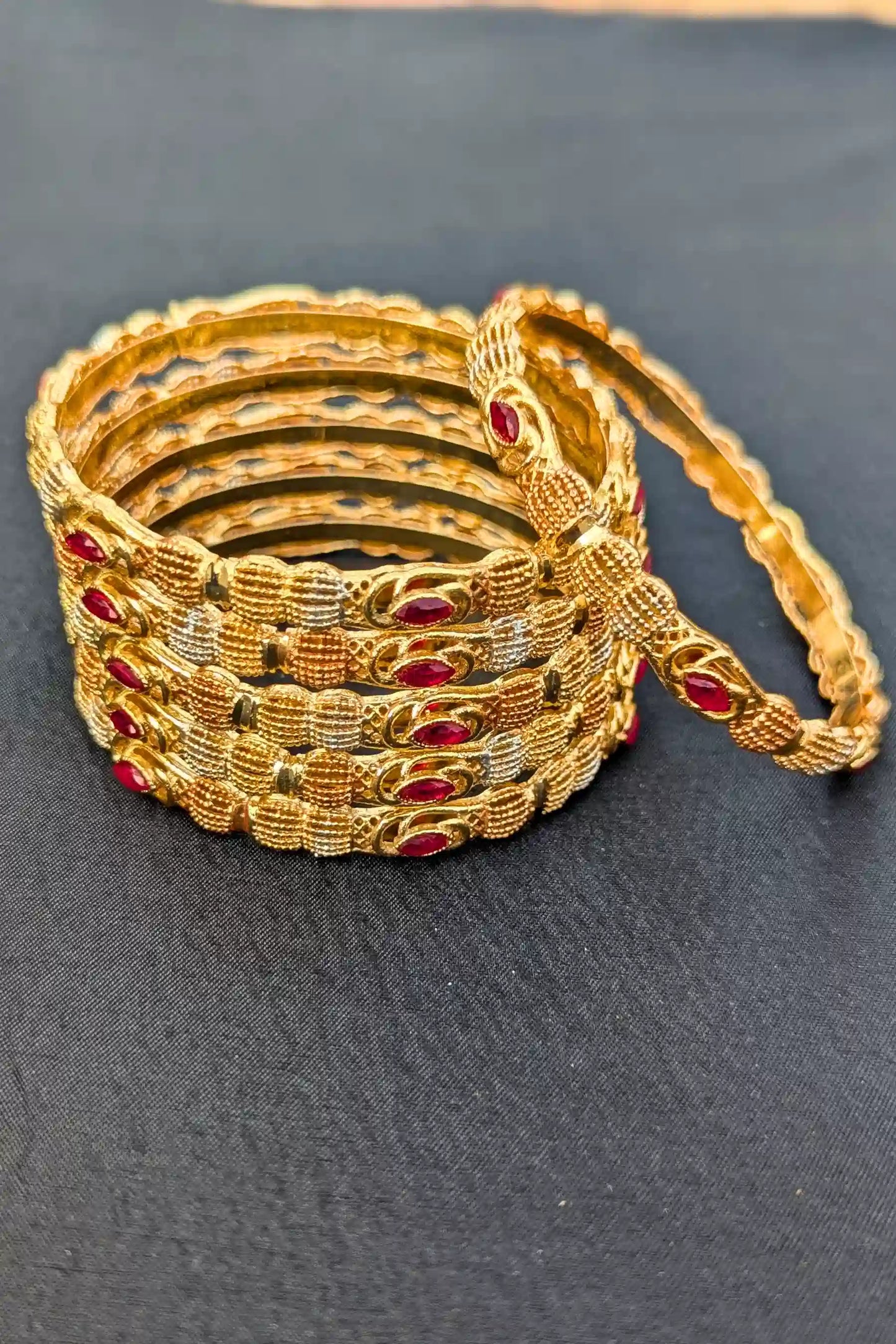 Set of gold bangles with red stones on a dark surface