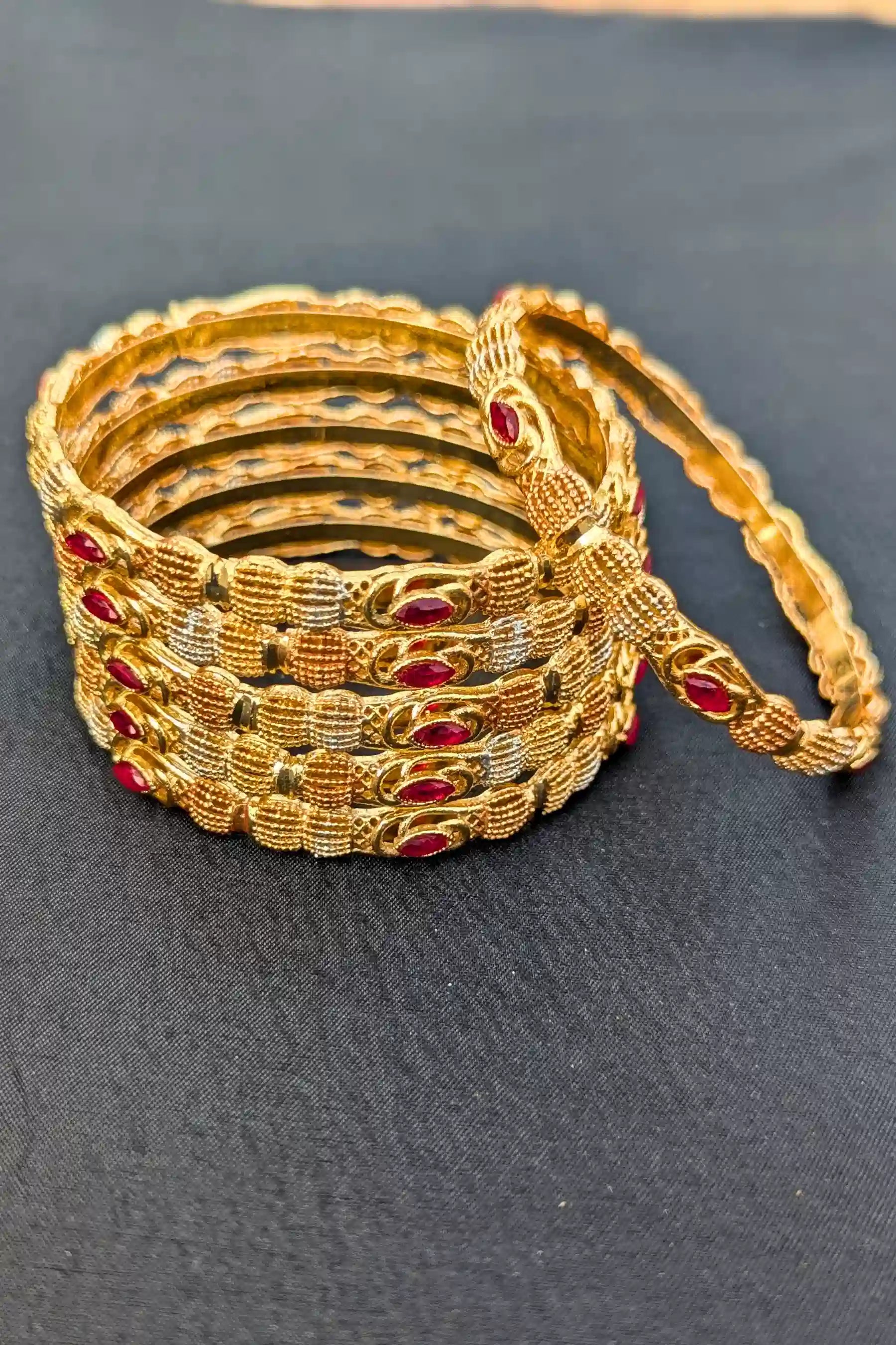 Set of gold bangles with red stones on a dark surface