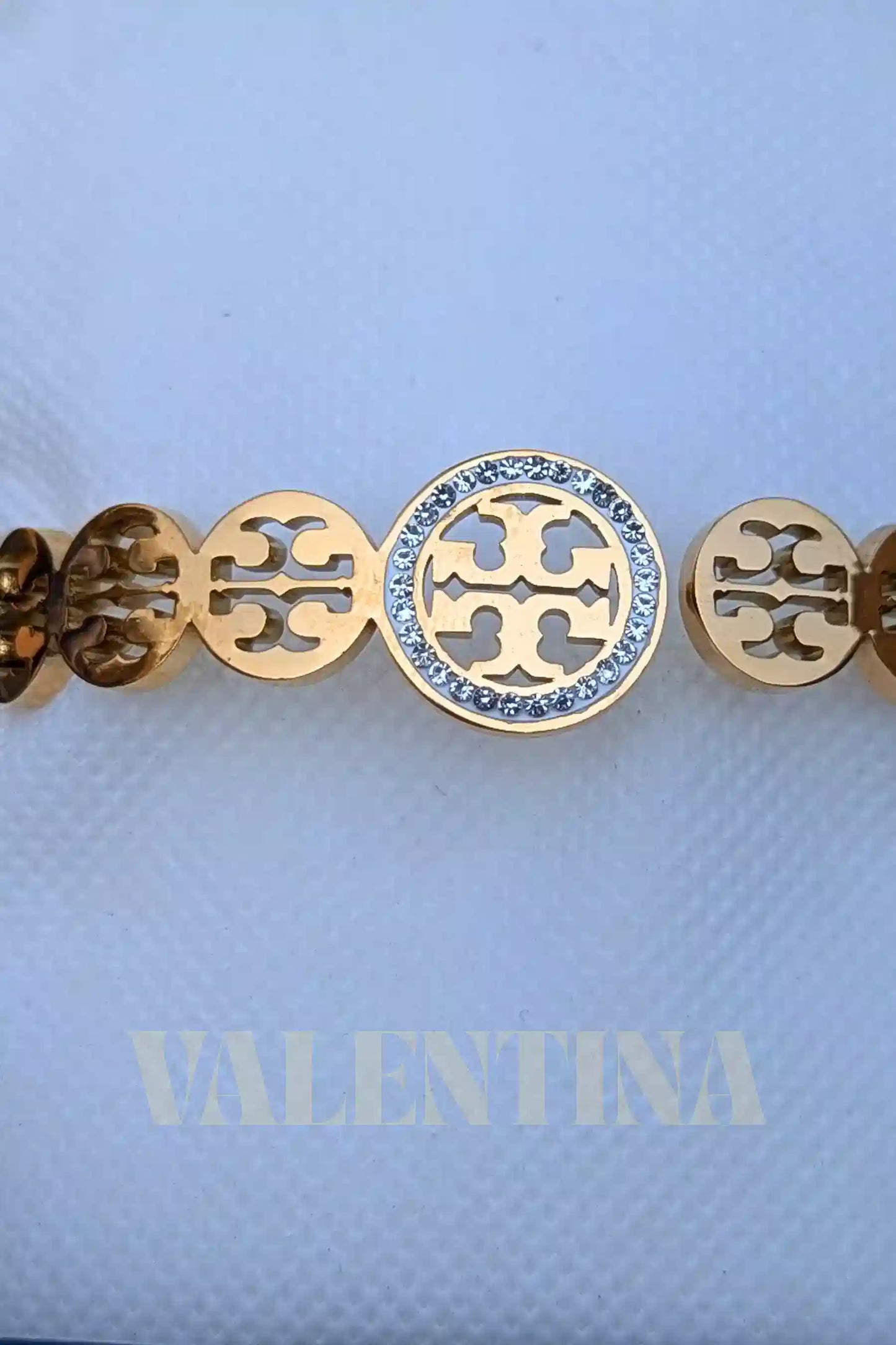 Gold bracelet with a central roundel and circular cut-out design on a light blue background with 'VALENTINA' branding.