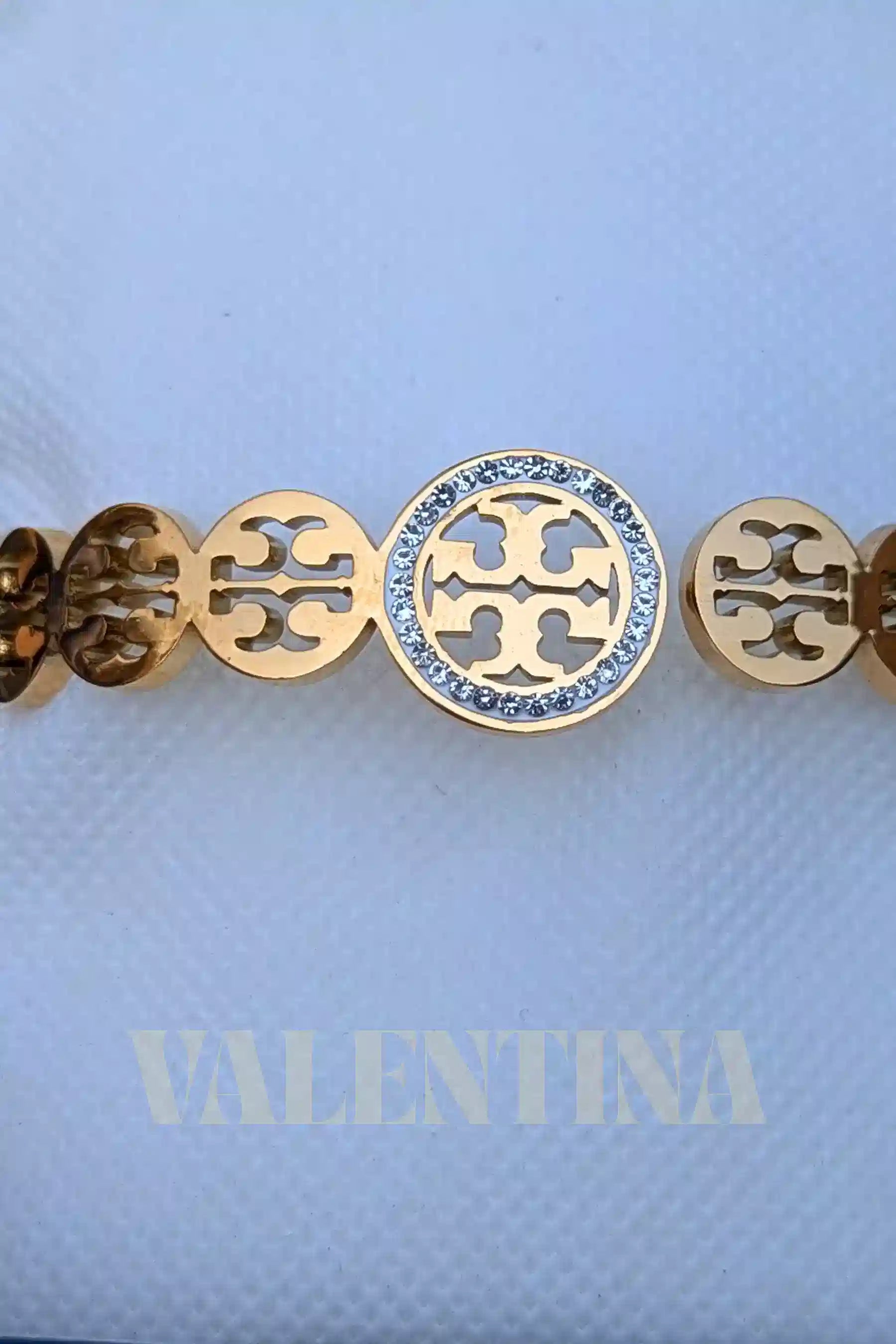Gold bracelet with a central roundel and circular cut-out design on a light blue background with 'VALENTINA' branding.
