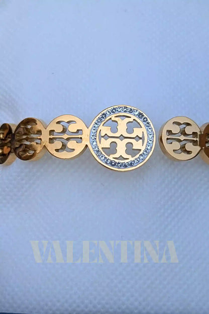 Gold bracelet with a central roundel and circular cut-out design on a light blue background with 'VALENTINA' branding.